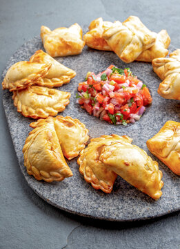 Cocktail empanadas on stone plate with tomato sauce and guacamole . Gray background. Latin American and Spanish tipical food
