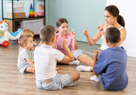 Kindergarten teacher reading to children in kindergarten. Children listen attentively to lessons, engaged in learning activities together. Joyful diverse kids in class.