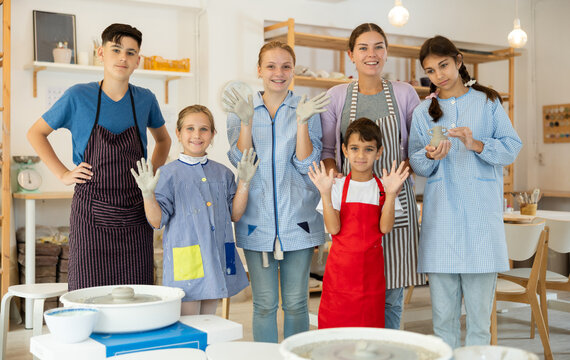 Happy children of different ages posing with young female teacher in pottery workshop