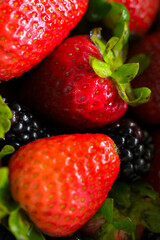 Macro shot of organic red strawberries with green leaves and dark berries © Yevg45