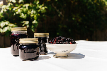 jam jars and blackberries in a bowl with summer garden background © Christina