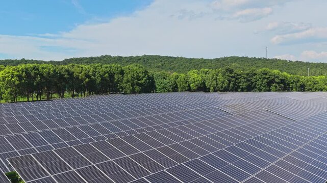 Aerial view gliding above solar panels and a dense forest