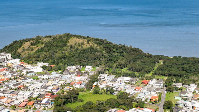 Reserva do Sahy, Condado, featuring modern residential houses nestled between lush green hills and the calm ocean waters in Mangaratiba, Rio de Janeiro, Brazil. Aerial view.