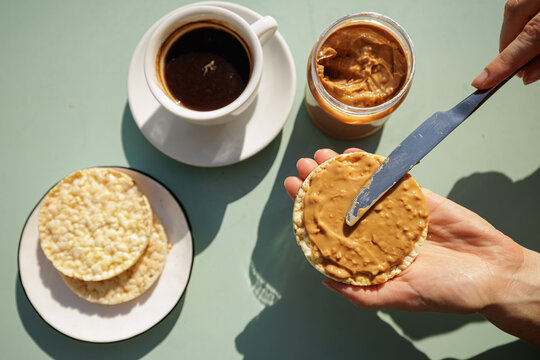 Hand Spreading Peanut Butter On Rice Cake For Light Breakfast