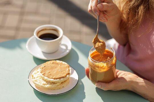 Spreading Peanut Butter On Rice Cakes With Coffee Outdoors