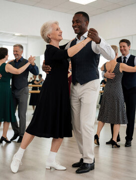 Mature interracial couple dances waltz in bright studio. Happy senior woman, black man perform ballroom moves. Elegant seniors enjoy hobby class together with diverse partners. People wear formal
