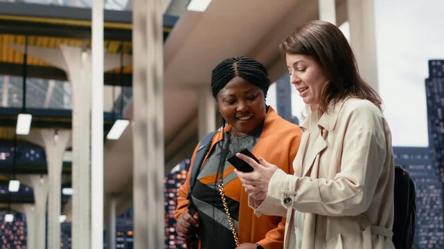 Close-up footage shows female tourists looking at a smartphone together while walking through the bus terminal, checking the shuttle departure timetable on the mobile phone inside the coach station.