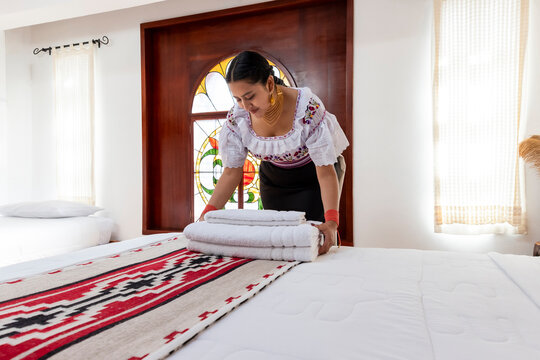 Indigenous Kichwa woman in traditional clothing arranging fresh white towels on a bed in a hotel room