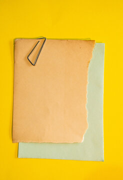 Papel rasgado beige sobre hojas pastel con clip met&aacute;lico y fondo amarillo