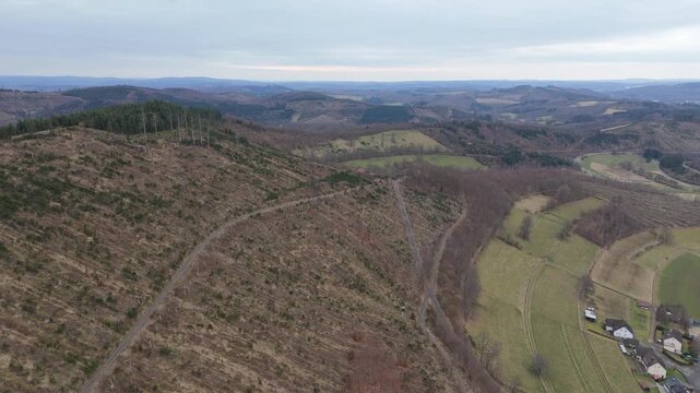 Push in aerial drone shot over the Elme mountain in North Rhine-Westphalia, Germany, with deforested hills and green fields.
