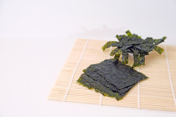 Dried seaweed rests on bamboo mat. One pile rests in a small bowl, slightly curled. Simple, clean, and natural presentation. Ideal for health or Asian cuisine contexts. No people, no animals, no brand © Nurma