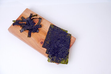 Dried crispy seaweed rests on a wooden board. Plates showcase texture and color, natural and rustic. Simple background highlights the seaweed's earthy tones. Perfect for food, health © Nurma