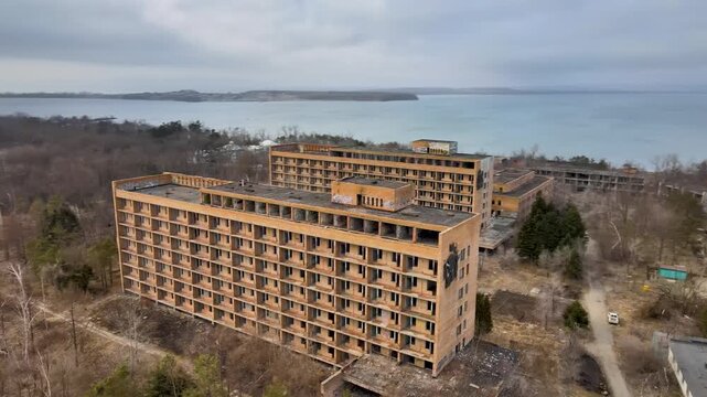 Aerial drone footage circling the abandoned buildings of the Sadgorod Mud Treatment Clinic near Vladivostok, Russia. The moving view reveals multiple old Soviet-era buildingsand  surrounding grounds.