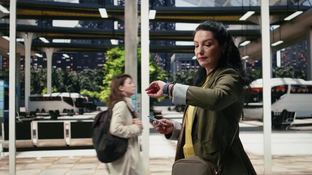 Traveler takes a ticket from her bag and checks the departure time while walking in a bus station; the passenger looks at her wristwatch to avoid being late.
