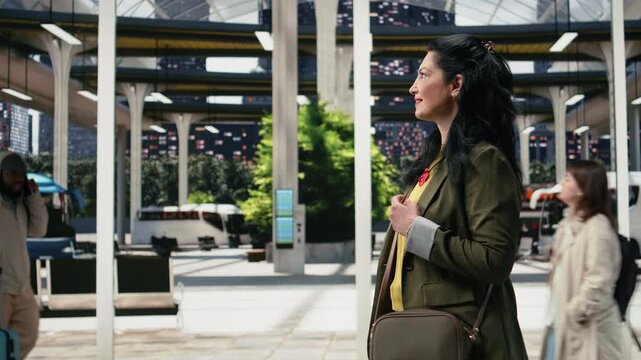 Woman walks through a bus terminal while searching for the correct departure platform before her coach arrives; the solo traveler navigates the public transport hub for an intercity journey.