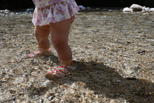 透明な川でサンダルを履いて入る1歳の子どもの足元。清流の浅瀬