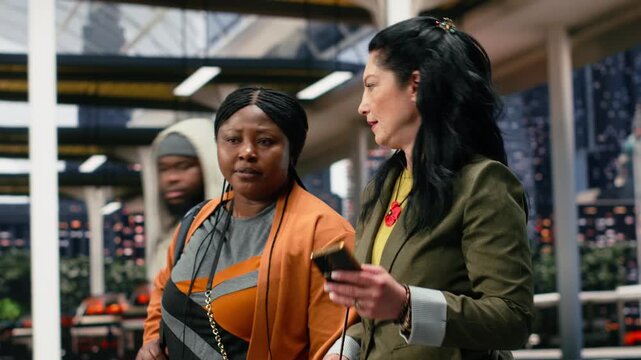Travel companions use a smartphone in the bus station to confirm trip details before coach departure, walking together through the shuttle terminal while checking the journey timetable on the phone.