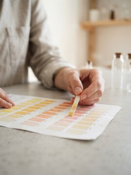 Woman comparing a pH test strip with a color chart to measure acidity levels in a laboratory