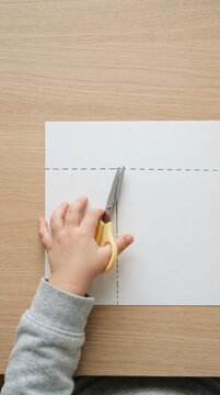 Toddler cutting paper with safety scissors practicing fine motor skills at wooden table