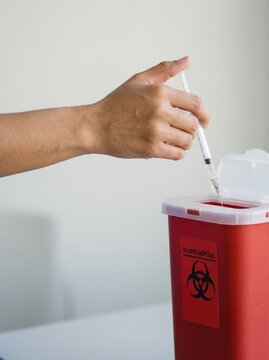 Person disposing of a medical syringe in a red sharps container representing safe healthcare waste management