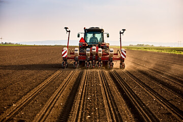 Obraz premium Farmer seeding field with tractor, preparing soil for new crop season