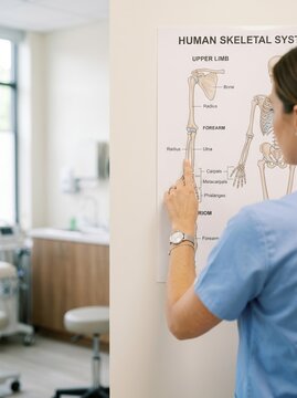 Female nurse pointing at a human skeletal system chart in a medical clinic room