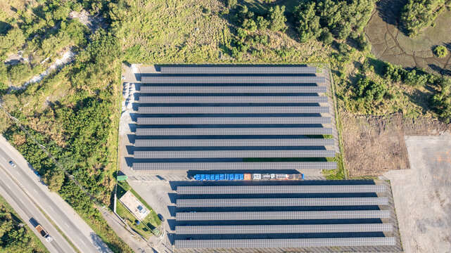 Large solar farm with rows of photovoltaic panels set against a backdrop of lush green forest and distant mountains in Itaguai, Rio de Janeiro, Brazil. Aerial view.