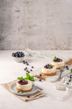 Mini cheesecakes with blueberry topping and mint leaves on a white rustic surface