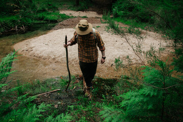 Hiker with Wooden Walking Stick Stepping Across Forest Stream Sandbar © Maria Sap
