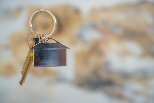 House keys with a house shaped keychain hanging on a wall hook. Concept of buying real estate, moving into a new home and property ownership.