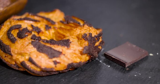 Brown chocolate striped cookie on black stone board, sweet pastry cookies ring next to dark chocolate block piece on kitchen table