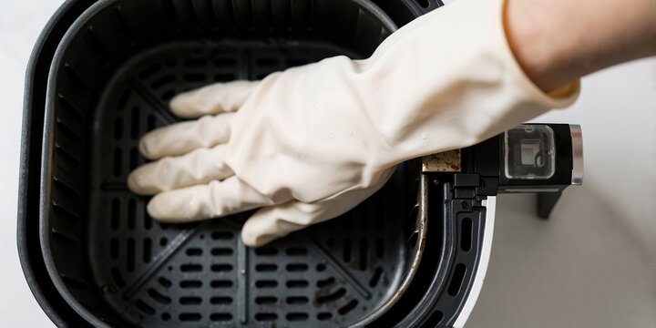 Gloved hand cleaning an air fryer basket in a kitchen setting representing household appliance maintenance