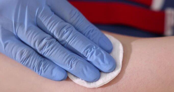 Doctor pressing cotton pad onto woman's arm with puncture site after blood draw in hospital, closeup