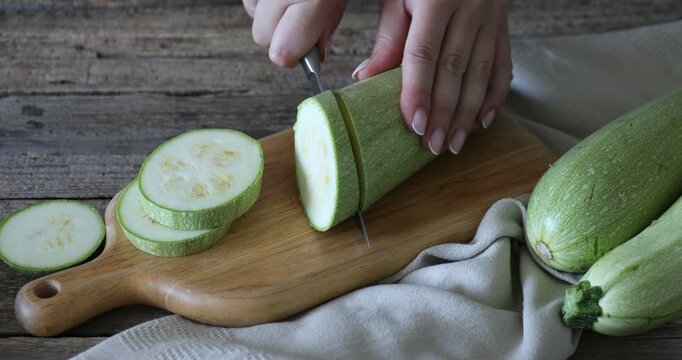 Woman cutting fresh zucchini at wooden table, closeup