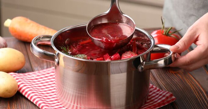 Woman taking tasty borscht from pot with ladle at wooden table, closeup