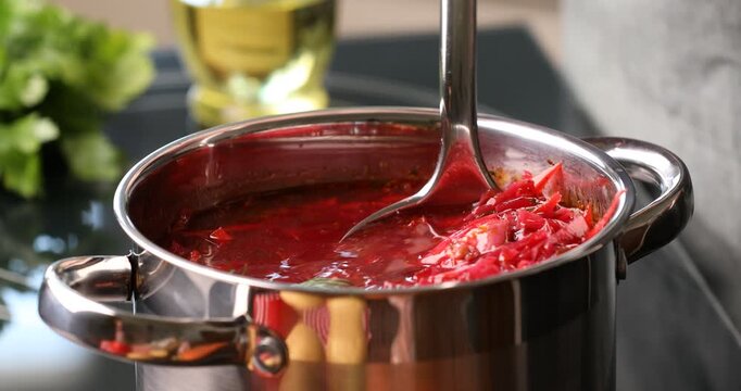 Woman taking borscht from pot with ladle at stove, closeup
