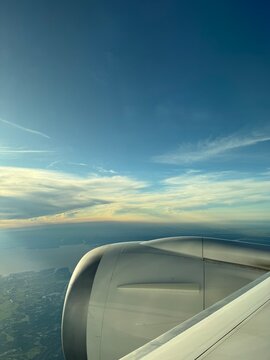 Airplane jet engine view from window flying over coastline at sunset