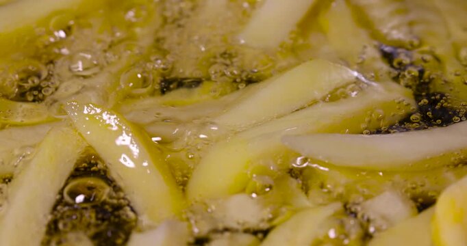 Slices of potato french fries frying in boiling oil, yellow french fries cooking inside deep fryer pan filled with hot liquid fat