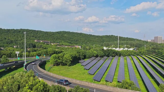 Aerial view moving over solar panels beside a highway curve