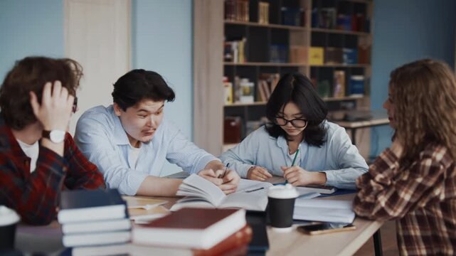 Students studying together at a table in a classroom with books notebooks and laptops