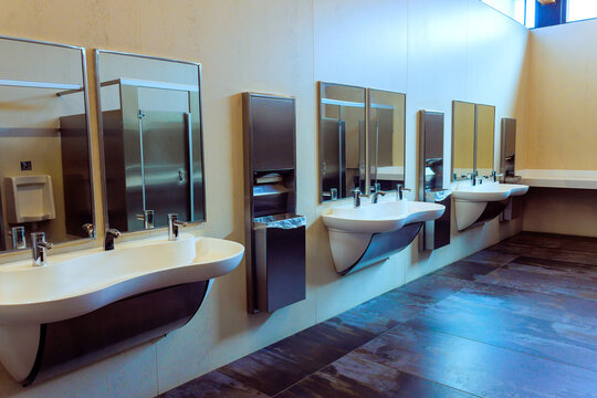 Restroom with several sinks, mirrors bright lights highlight clean design in public area.