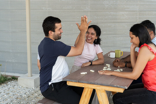 Young adults playing dominoes at outdoor table, giving high five