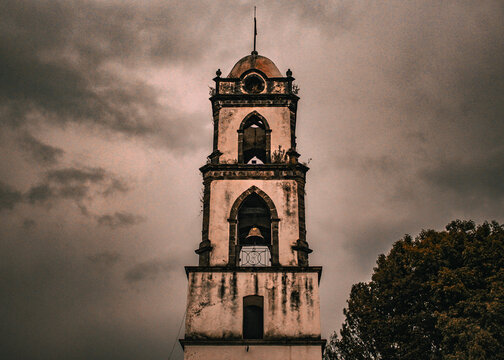 Historic colonial church bell tower against a dramatic cloudy sky
