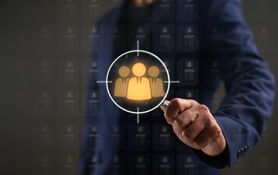A businessman targets a specific group of people, symbolizing focused recruitment or audience targeting using a magnifying glass and digital icons.