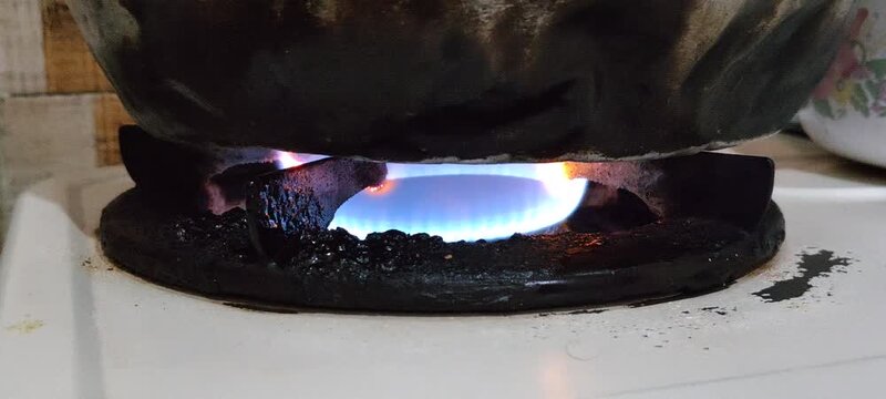 Close up of a blue gas flame burning under a dark pot.