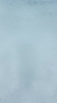 Vertical video of heavy rain drops splashing on blue swimming pool water during thunderstorm in Miami