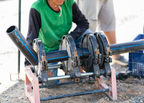 A technician operating a butt fusion welding machine to join black HDPE pipes on an outdoor construction site.