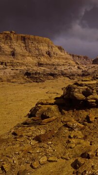 Vivid scenery of a vast desert showcases grand rock formations bathed in golden hues. Dark clouds loom above, creating a dramatic atmosphere filled with contrasting colors.