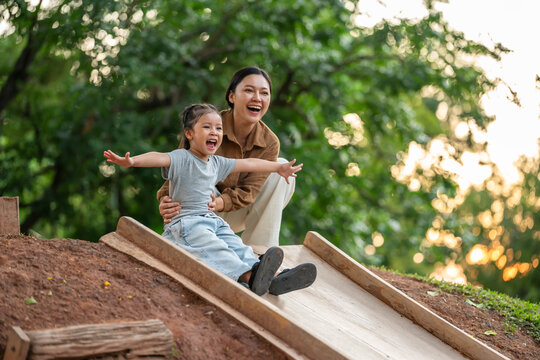 happy mother and preschool child girl sliding and playing at playground