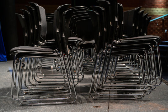 A close-up view of neatly stacked black chairs under soft stage lighting, showcasing their sleek design and organized arrangement in a performance space.